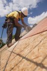 Charpentier utilisant une scie circulaire sur le panneau de toit d'une maison en construction — Photo de stock