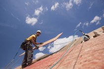 Carpintero instalando panel en forma de L en el techo de una casa en construcción - foto de stock
