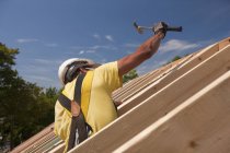 Carpinteiro hispânico usando um martelo na cobertura em uma casa em construção — Fotografia de Stock