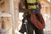 Un charpentier hispanique enroule un cordon d'alimentation électrique sur un chantier — Photo de stock