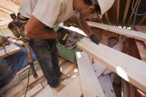 Carpinteiro hispânico usando uma serra circular em uma viga em uma casa de ângulo em construção — Fotografia de Stock