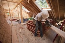 Carpenter using a circular saw on the roof rafter at a house under construction — Stock Photo