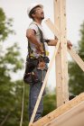 Carpinteiro hispânico examinando postes de chaminé em uma casa em construção — Fotografia de Stock