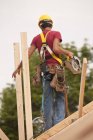 Carpinteiro hispânico usando uma serra circular no telhado em uma casa em construção — Fotografia de Stock