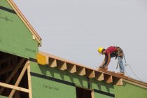 Charpentier hispanique mesurant un panneau de toit d'une maison en construction — Photo de stock