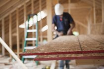 Carpinteiro usando uma serra circular em placa de partículas em uma casa em construção — Fotografia de Stock