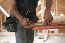 Carpintero hispano midiendo un panel de techo de una casa en construcción - foto de stock