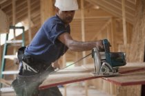 Carpinteiro hispânico cortando o painel do telhado com uma serra circular em uma casa em construção — Fotografia de Stock