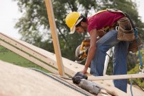 Carpinteiro hispânico usando uma serra circular no telhado em uma casa em construção — Fotografia de Stock