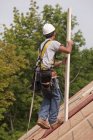 Falegname ispanico che trasporta assi sul tetto di una casa in costruzione — Foto stock