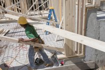 Tischler trägt eine Planke auf einer Baustelle — Stockfoto