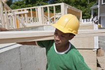Tischler trägt eine Planke auf einer Baustelle — Stockfoto