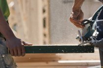 Carpinteros sierra viga en un sitio de construcción de edificios - foto de stock