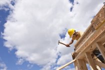 Carpintero martillando en las vigas del piso superior en un sitio de construcción de edificios - foto de stock