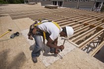 Carpenter hammering particle board in place at a building construction site — Stock Photo
