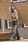Carpintero que lleva un tablero de partículas en un sitio de construcción de edificios - foto de stock