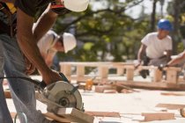 Carpenters using circular saw at a construction site with gable frame in the background — Stock Photo