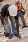 Carpenter nailing two studs together with a nail gun at a building construction site — Stock Photo