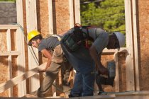 Carpinteiro de elevação pregos e usando pistola de prego em um canteiro de obras de construção — Fotografia de Stock