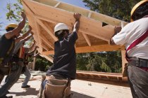 Charpentiers soulevant le cadre à pignon de toiture sur un chantier de construction — Photo de stock