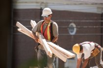 Carpinteros llevando tablones de madera en un sitio de construcción - foto de stock