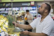 Man with Down Syndrome weighing pineapple in a grocery store — Stock Photo