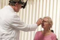 Oftalmólogo examinando los ojos de una mujer con un oftalmoscopio indirecto - foto de stock