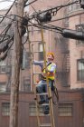 Cable lineman subindo uma escada no poste de energia da cidade — Fotografia de Stock