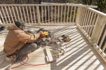 Carpinteiro hispânico usando serra de corte para cortar a tampa de corrimão deck — Fotografia de Stock