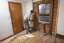 Латиноамериканский плотник, использующий реверсивную пилу для удаления окна и разрезания дверного проема — стоковое фото