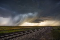 Dark storm clouds over railroad tracks in a field with rain falling in the distance; Marquis, Saskatchewan, Canada — Stock Photo