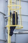 Female power engineer climbing inside safety cage ladder at power station — Stock Photo