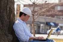 Китайский студент сидит под деревом с ноутбуком — стоковое фото