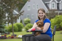 Jeune femme atteinte de paralysie cérébrale chevauchant le scooter avec son chien — Photo de stock