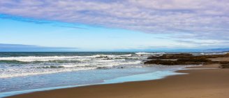 Puesta de sol sobre el Océano Pacífico a lo largo de la costa de Oregon con la marea arrastrándose sobre la arena; Oregon, Estados Unidos de América - foto de stock
