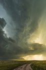 Supercell au-dessus des prairies et un chemin de terre, avec la lumière du soleil illuminant le ciel dramatique ; Tulsa, Oklahoma, États-Unis d'Amérique — Photo de stock