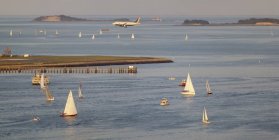 Barcos de recreo en Boston Harbor con aterrizaje de aviones en Logan Airport, Boston, Massachusetts, EE.UU. - foto de stock