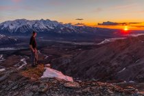 Ein Wanderer beobachtet den Sonnenuntergang von einem Bergrücken in der Alaska Range; Alaska, Vereinigte Staaten von Amerika — Stockfoto