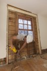 Carpinteiro hispânico usando serra recíproca para cortar moldura de parede através do acesso à janela — Fotografia de Stock