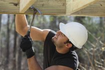Hispanic carpenter nailing pressure treated deck joist with hammer — Stock Photo