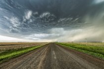 Gravel road leading into the distance towards dramatic storm clouds; Val Marie, Saskatchewan, Canada — Stock Photo