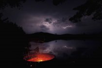 Табор вогняної ями вночі з блискавкою на задньому плані на озері Umbagog, Нью-Гемпшир, Уса — стокове фото