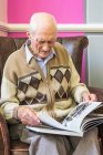 Älterer Mann sitzt auf einem Stuhl und betrachtet ein Buch über den Zweiten Weltkrieg; Hartlepool, County Durham, England — Stockfoto