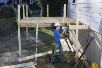 Carpenter using nail gun to install deck joists on home — Stock Photo