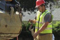 Trabajador de construcción adjuntando correa de elevación al cubo de la excavadora - foto de stock