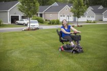 Giovane donna con paralisi cerebrale cavalcando il suo scooter sul suo prato — Foto stock