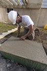 Hispanic carpenter using finish trowel to roughen stairway footing concrete — Stock Photo