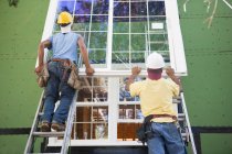 Carpenters positioning a large window frame on a house under construction — Stock Photo