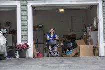 Mujer joven con parálisis cerebral subiendo a su scooter en el garaje - foto de stock