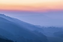 Silhouetted layers of hills and a colourful sunset through fog in South Downs National Park; Brighton, East Sussex, England — Stock Photo